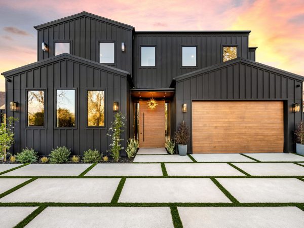Modern black house exterior with wooden garage door and driveway at sunset.